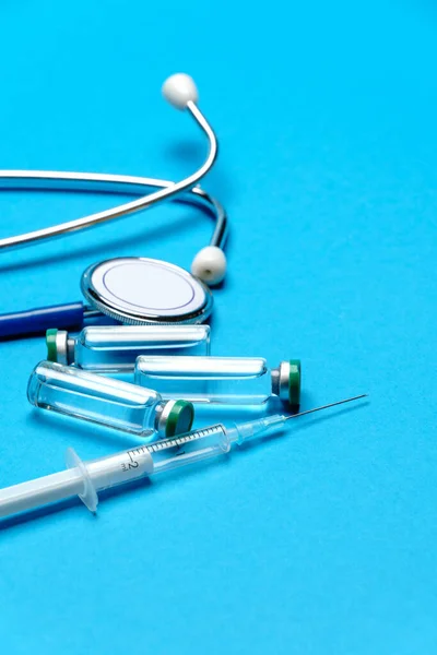 Stethoscope, syringe and ampoules with medicines or vaccine over blue background — Stock Photo, Image