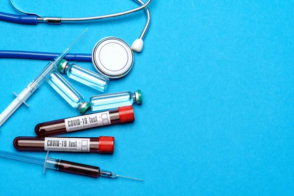 Stethoscope, syringe, test tubes with blood samles and ampoules with medicine or vaccine over blue background — Stock Photo, Image