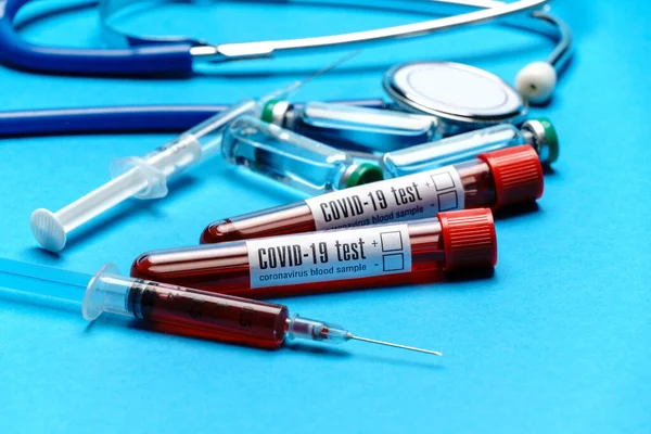Stethoskop, Spritze, Reagenzgläser mit Blutproben und Ampullen mit Medikamenten oder Impfstoff vor blauem Hintergrund — Stockfoto