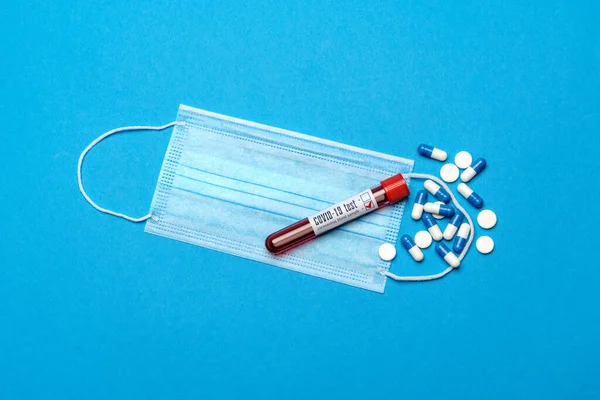 Védő orvosi arcmaszkok, kémcső vérmintával és tabletták kék alapon - Felülnézet másolási hellyel — Stock Fotó