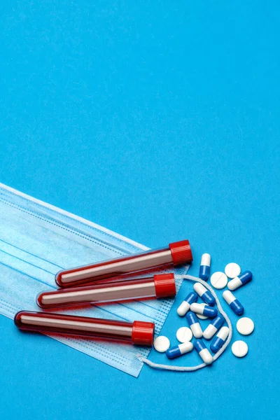 Védő orvosi arcmaszkok, kémcső vérmintával és tabletták kék alapon - Felülnézet másolási hellyel — Stock Fotó
