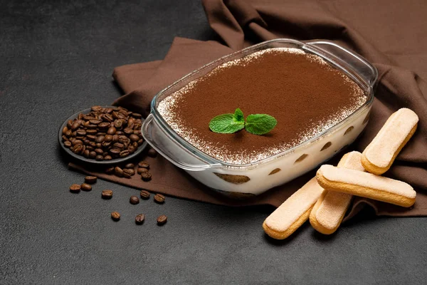 Traditional Italian Tiramisu dessert in glass baking dish and savoiardi cookies on concrete background — Stock Photo, Image