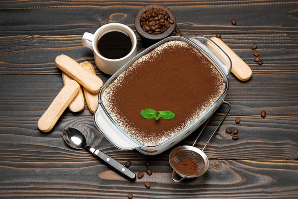 Traditionele Italiaanse Tiramisu dessert in glazen bakvorm, savoiardi koekjes en een kopje verse hete espresso koffie op houten achtergrond — Stockfoto
