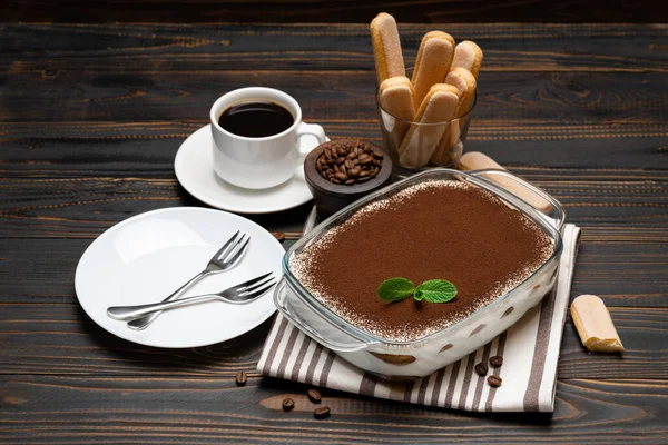 Traditionele Italiaanse Tiramisu dessert in glazen bakvorm, savoiardi koekjes en een kopje verse hete espresso koffie op houten achtergrond — Stockfoto