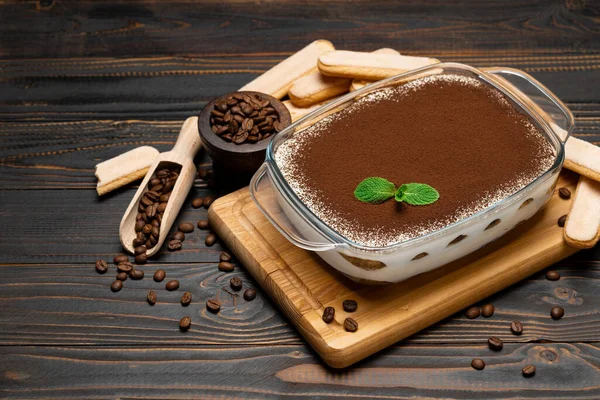 Traditioneel Italiaans Tiramisu dessert in glazen bakvorm en savoiardi koekjes op snijplank op houten ondergrond — Stockfoto