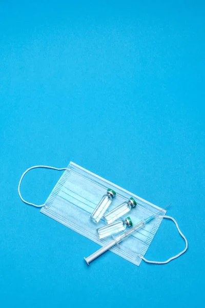 Spuit, beschermend medisch masker en ampullen met geneesmiddelen of vaccin op blauwe achtergrond — Stockfoto
