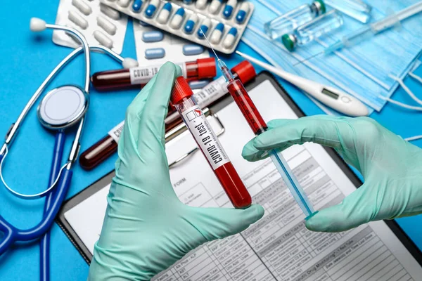 Labortechniker oder Arzt mit Gummi- oder Latexhandschuhen, die das Blutprobenröhrchen über Klemmbrett mit Blanko-Formular halten — Stockfoto