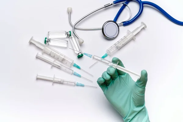 Lab technician assistant holding syringe over light grey or white background with medical ampoule vials, syringes and stethoscope — Stock Photo, Image