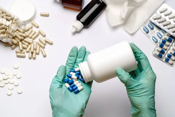 Close-up arts hand in een latex handschoen met capsules over lichtgrijze of witte achtergrond met medische benodigdheden — Stockfoto
