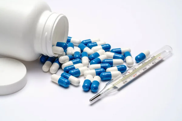 Medicijnen capsules in een fles en thermometer op lichtgrijze achtergrond — Stockfoto