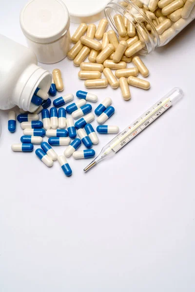 Medicijnen capsules in plastic flessen en thermometer op lichtgrijze achtergrond — Stockfoto