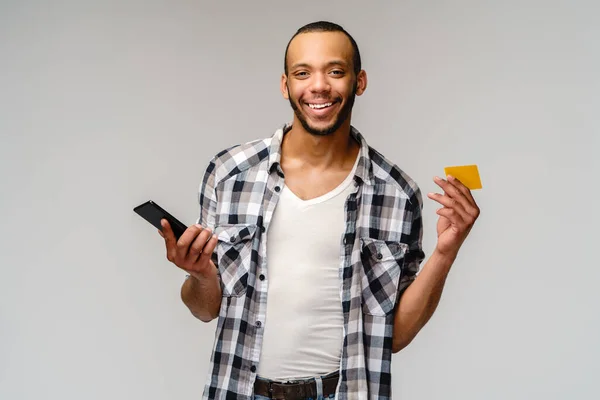 Jeune homme afro-américain souriant et hoding carte de crédit et téléphone portable sur fond gris avec espace de copie — Photo