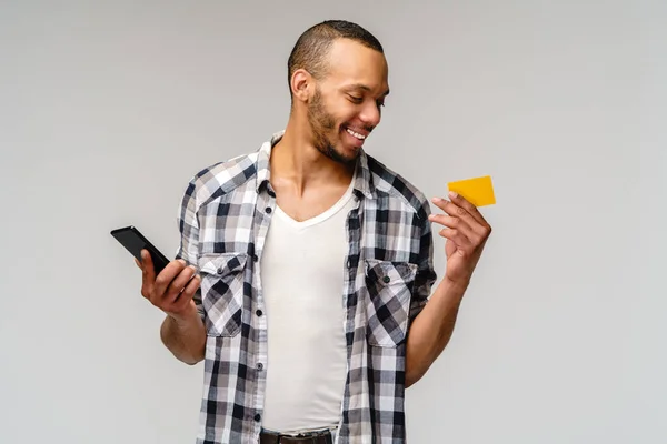 Jeune homme afro-américain souriant et hoding carte de crédit et téléphone portable sur fond gris avec espace de copie — Photo