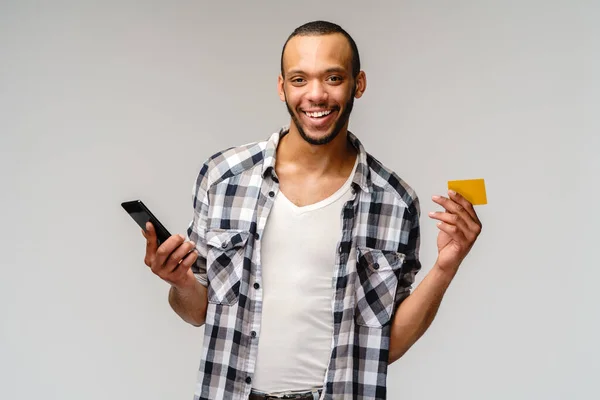 Jovem afro-americano sorrindo e encapuzando cartão de crédito e celular sobre fundo cinza com espaço de cópia — Fotografia de Stock