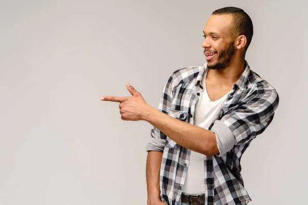 Joyful amigável afro-americano jovem iwearing camisa casual apontando por dedo para espaço de cópia vazio — Fotografia de Stock