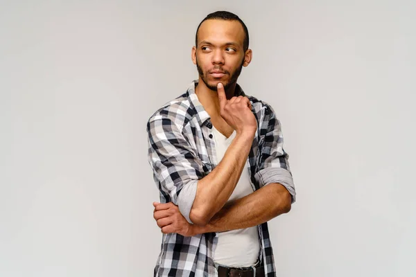 Close-up portret van jonge Afrikaans-Amerikaanse man denken dagdromen diep over iets vinger op de lippen weg te kijken over grijze achtergrond — Stockfoto