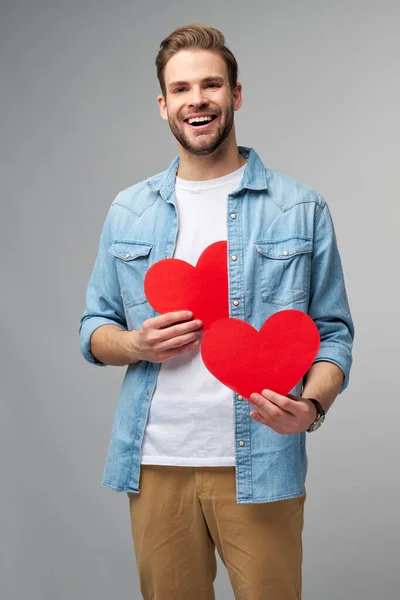 Retrato de hombre encantador de la mano de papel en forma de corazón de la tarjeta de desgaste camisa de estilo casual aislado sobre fondo gris — Foto de Stock