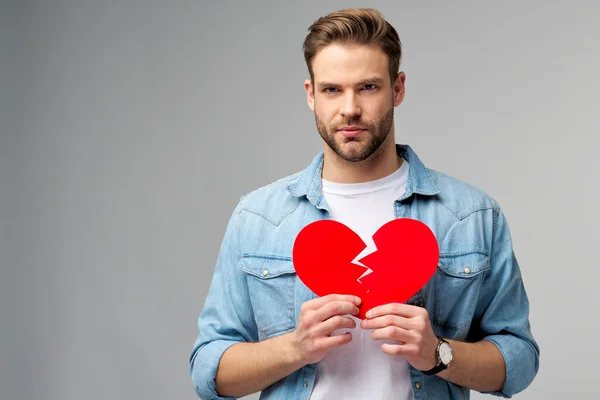Joven guapo sosteniendo papel roto rojo corazón de San Valentín de pie sobre fondo gris —  Fotos de Stock