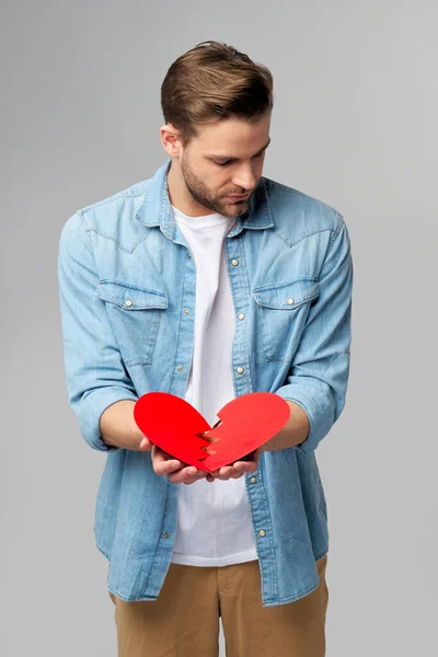 Kırık kağıt tutan yakışıklı genç adam Gri arka planda duran kırmızı sevgililer günü kalbi — Stok fotoğraf