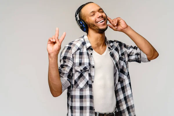 Giovane uomo afroamericano in ascolto di musica su grandi auricolari in piedi su sfondo grigio chiaro — Foto Stock