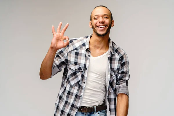 Jovem afro-americano vestindo camisa casual e mostrando ok sinal sobre fundo cinza claro — Fotografia de Stock