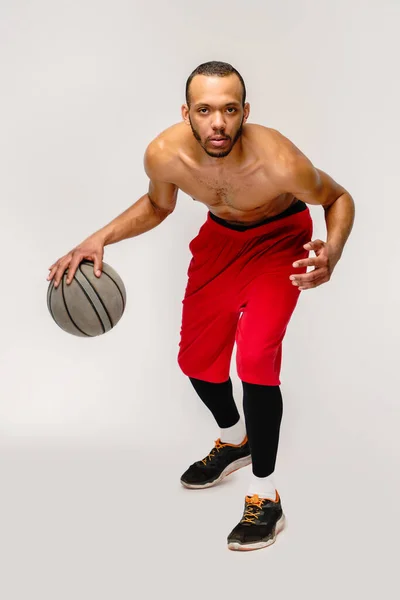 Muskulöser afrikanisch-amerikanischer Sportler beim Basketballspielen auf hellgrauem Hintergrund — Stockfoto