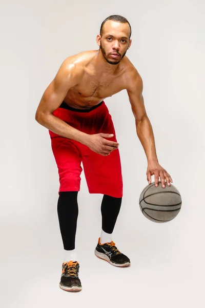 Мускулистый американский спортсмен, играющий в баскетбол на светло-сером фоне — стоковое фото