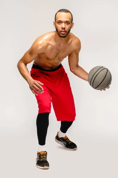 Muskuløs amerikansk idrettsmann som spiller basketball på grunn av lysegrå bakgrunn – stockfoto
