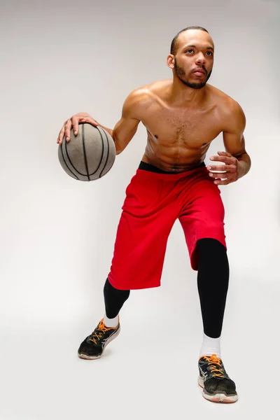 肌肉发达的非洲裔美国运动员，在浅灰的背景下打篮球 — 图库照片
