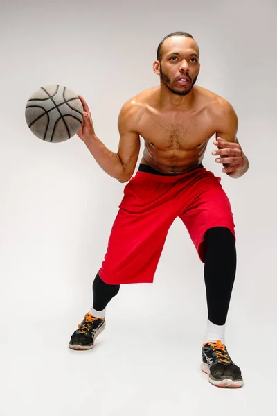 Muskularny afrykański sportowiec gra w koszykówkę srając na jasnoszarym tle — Zdjęcie stockowe