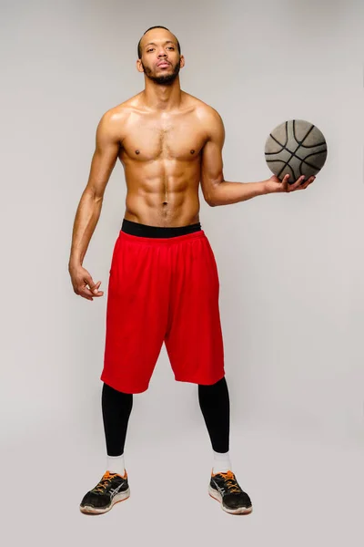 Izmos afro-amerikai sportoló kosárlabda szarul játszik világosszürke háttér — Stock Fotó