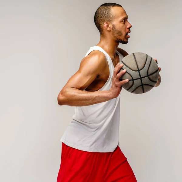 ライトグレーの背景の上にバスケットボールをしている筋肉アフリカ系アメリカ人のスポーツマン — ストック写真