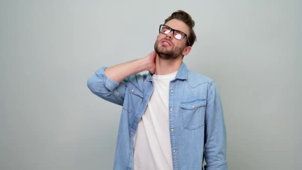 Bärtiger Typ im Jeanshemd sieht erschöpft aus, reibt sich schmerzenden Nacken — Stockvideo