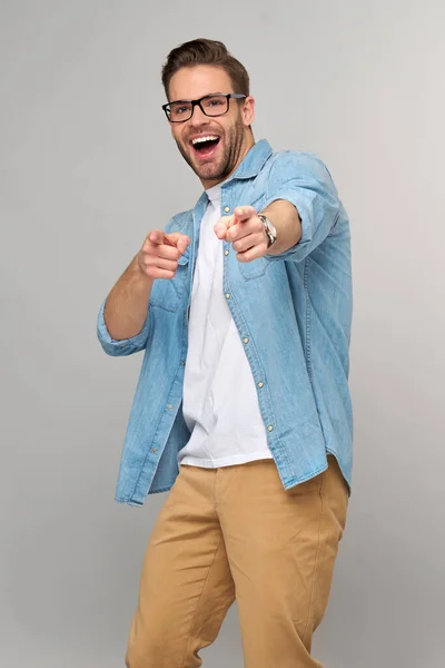 Glücklicher junger gutaussehender Mann in Jeanshemd, der vor grauem Hintergrund auf die Kamera zeigt — Stockfoto