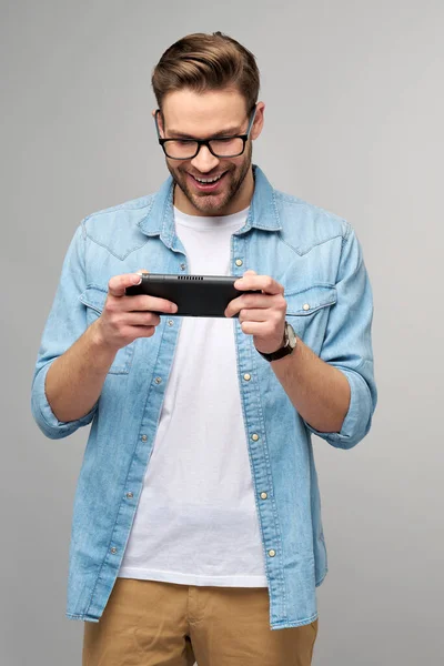 Giovane uomo handcome giocare con portatile videogioco in piedi su sfondo grigio — Foto Stock