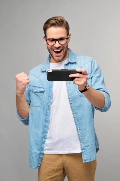 Giovane uomo handcome giocare con portatile videogioco in piedi su sfondo grigio — Foto Stock