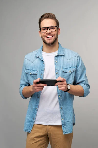 Junger Mann spielt mit tragbarem Videospiel vor grauem Hintergrund — Stockfoto