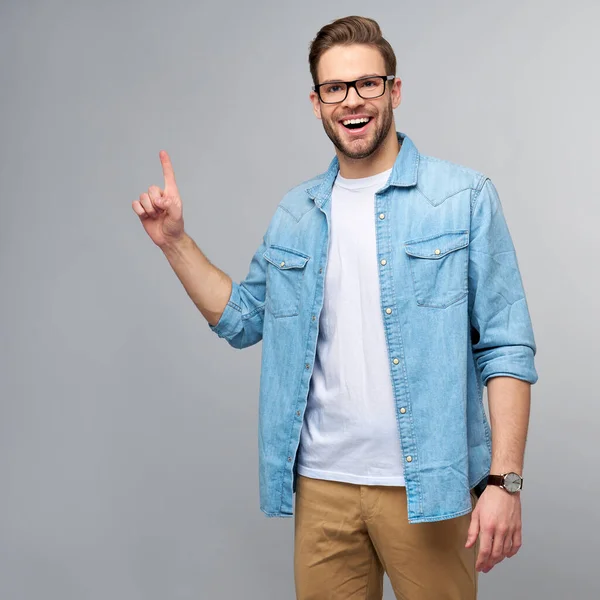 Glücklicher junger gutaussehender Mann in Jeanshemd, der vor grauem Hintergrund wegzeigt — Stockfoto