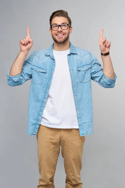 Glücklicher junger gutaussehender Mann in Jeanshemd, der vor grauem Hintergrund wegzeigt — Stockfoto