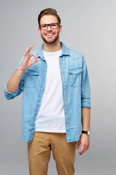 Portrait of young handsome caucasian man in jeans shirt shows ok sign gestur standing over light background — Stok Foto