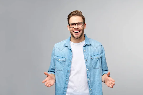 Ung man bär jeans skjorta välkomnar dig med ett leende på ansiktet och hans armar vidöppen stående över grå bakgrund — Stockfoto