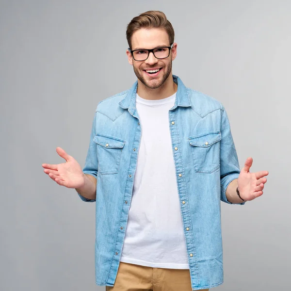 Jonge man draagt jeans shirt verwelkomen u met een glimlach op zijn gezicht en zijn armen wijd open staande over grijze achtergrond — Stockfoto