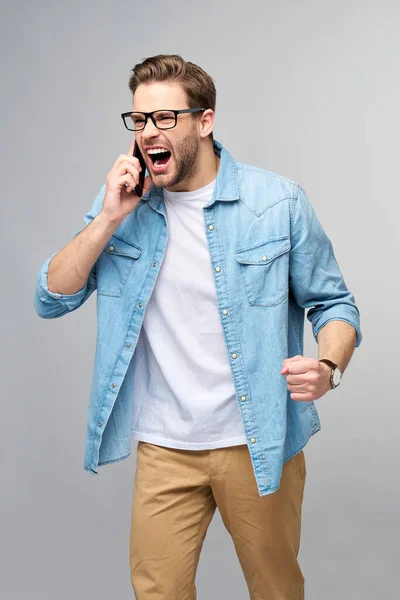 Ziemlich lässiger Mann in blauem Jeanshemd, der sein Handy über dem grauen Hintergrund des Studios hält — Stockfoto