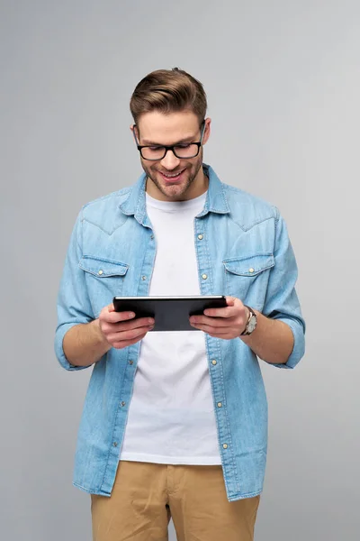 Feliz joven con camisa vaquera de pie y tableta sobre fondo gris estudio — Foto de Stock