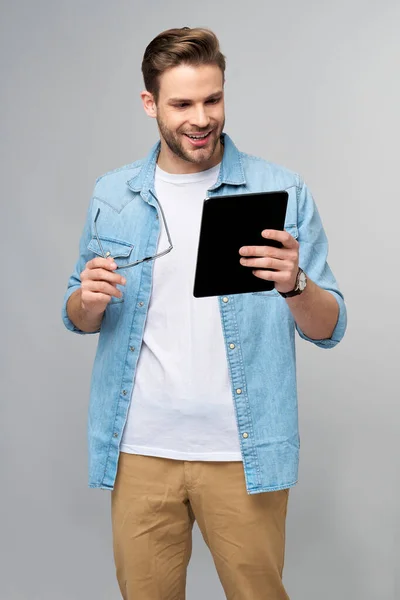 Feliz joven con camisa vaquera de pie y tableta sobre fondo gris estudio — Foto de Stock