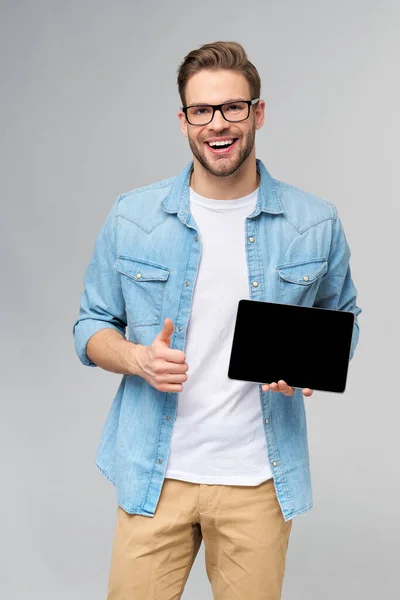 Jeune homme heureux portant chemise jeans debout et tenant tablette pc pad sur fond gris studio — Photo