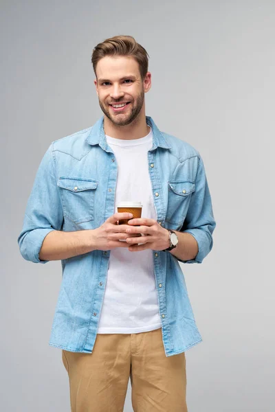 Portrait de jeune homme caucasien beau en jeans chemise sur fond clair tenant tasse de café à emporter — Photo