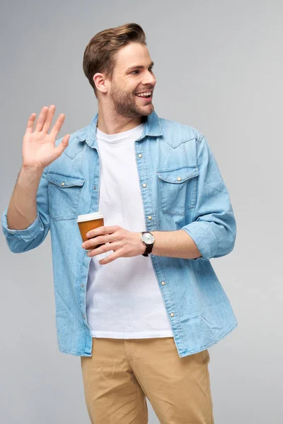 Retrato de joven guapo hombre caucásico en jeans camisa sobre fondo claro sosteniendo taza de café para llevar —  Fotos de Stock