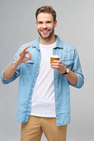 Retrato de jovem caucasiano bonito em camisa jeans sobre fundo claro segurando xícara de café para ir — Fotografia de Stock