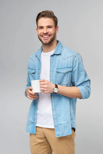 Porträtt av ung vacker kaukasisk man i jeans skjorta över ljus bakgrund innehav kopp kaffe — Stockfoto